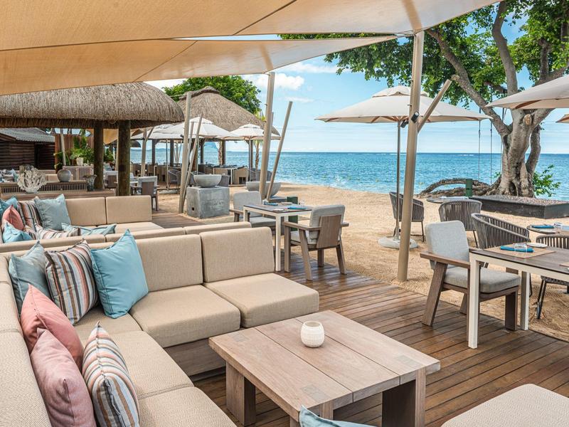 Offenes Strandrestaurant mit bequemen Sesseln, Holzterrasse und Blick auf das blaue Meer.