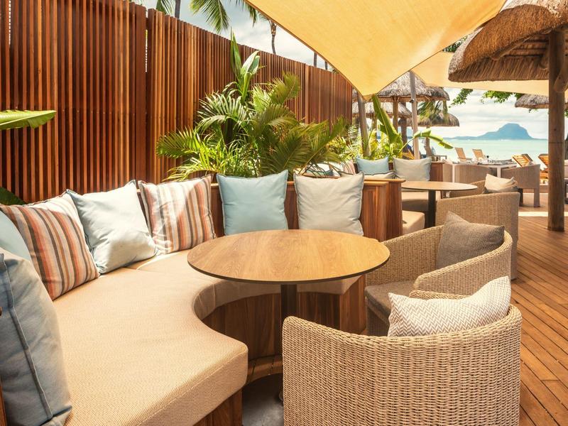 Gemütliche Outdoor-Lounge mit Rundtisch, Polstersofa, Stühlen, Holzboden und Sonnenschutz.