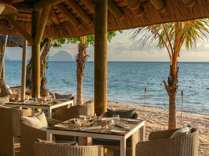 Strandrestaurant mit gedeckten Tischen, Holzdach und Blick aufs Meer bei Sonnenuntergang.