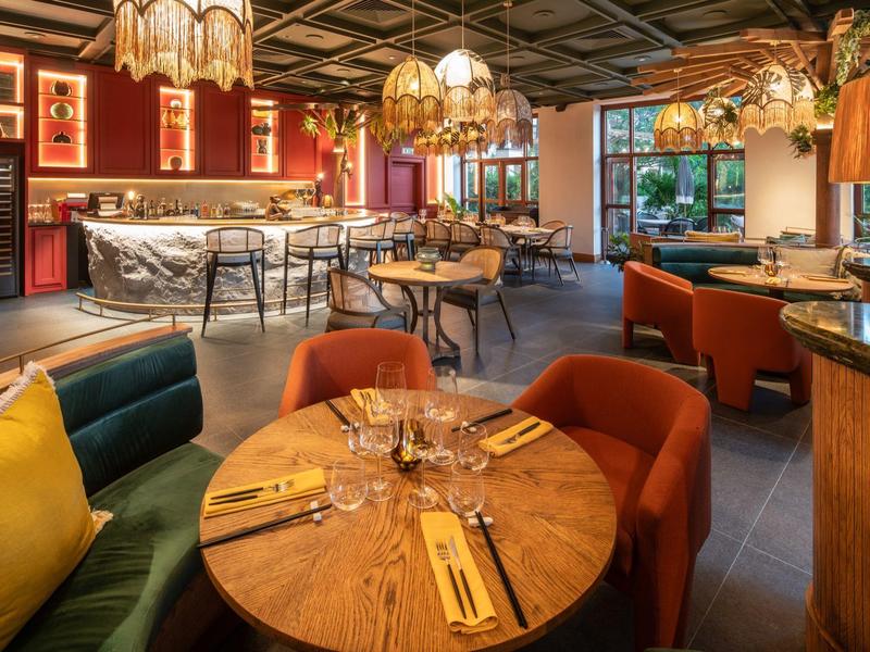 Gemütliches Restaurant mit warmem Licht, Holztischen, bunten Sesseln und moderner Deckenbeleuchtung.