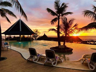 Poolbereich mit Liegestühlen, Palmen und Sonnenuntergang am Meer in einem Hotel.