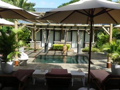 Hotelterrasse mit Sonnenschirmen, Liegestühlen und tropischen Pflanzen neben einem Wasserbecken.