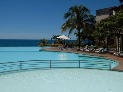 Infinity-Pool mit Liegestühlen und Palmen an einem Hotel mit Meerblick.