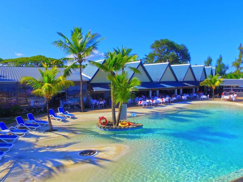 Schöner Außenpool mit klarem Wasser, blauen Liegestühlen und Palmen unter blauem Himmel.
