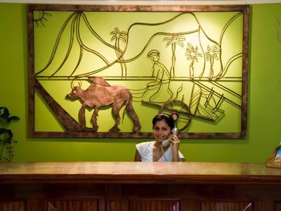 Rezeptionistin am hölzernen Empfangstresen vor grünem Wandbild mit Elefant und Palmen.