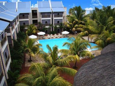 Hotelanlage mit zentralem Swimmingpool, umgeben von Palmen und Mehrfamiliengebäuden unter blauem Himmel.