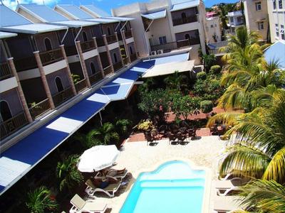 Espace extérieur d'un hôtel avec piscine, parasols et coins salon entourés de palmiers.
