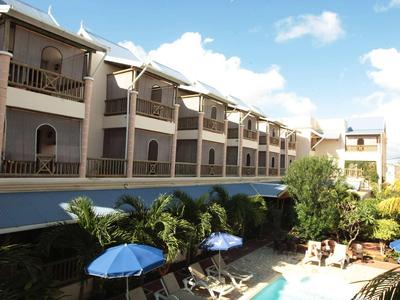 Hotelgebäude mit Balkonen, Poolbereich und blauen Sonnenschirmen unter klarem Himmel.