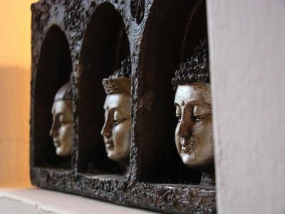 Trois têtes de Bouddha dorées dans des niches sombres sur un mur, éclairées chaleureusement.