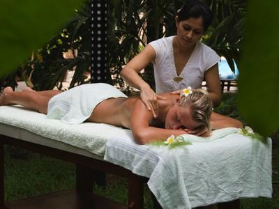 Femme recevant un massage sur une table extérieure entourée de plantes.