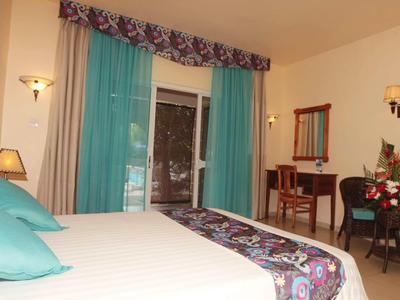 Chambre d'hôtel confortable avec grand lit, bureau et accès au balcon avec rideaux turquoise.