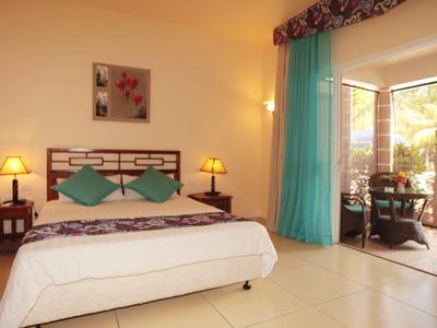 Chambre d'hôtel lumineuse avec lit double, tables de chevet et accès à un balcon avec vue sur le jardin.