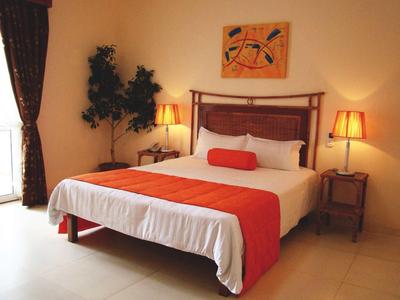 Chambre d'hôtel lumineuse avec grand lit, jeté orange et deux tables de chevet avec lampes.