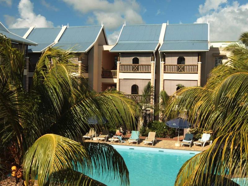 Hôtel avec chaises longues autour d'une piscine entourée de palmiers sous un ciel bleu.