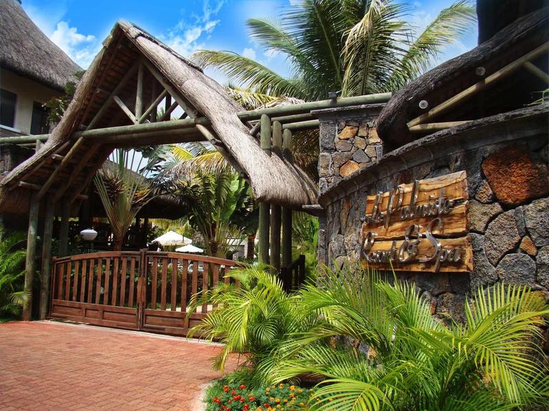 Entrée d'un lodge tropical avec une façade en pierre et des palmiers sous un ciel bleu.