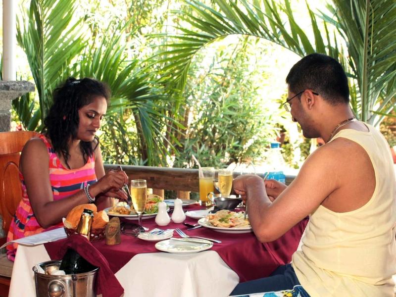 Couple prenant le petit déjeuner avec jus et café sur une terrasse avec des chaises en terre cuite et des plantes exotiques.