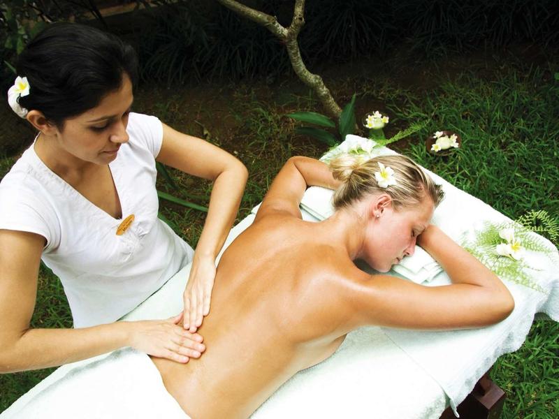 Une femme reçoit un massage sur une table en plein air dans un cadre de jardin verdoyant.