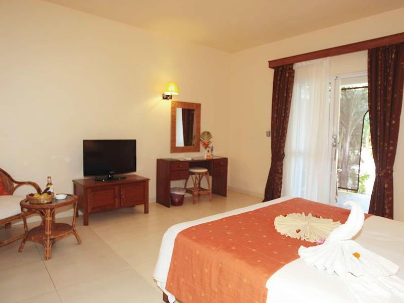 Chambre d'hôtel avec lit double, télévision, bureau, chaise et accès au balcon avec rideaux.