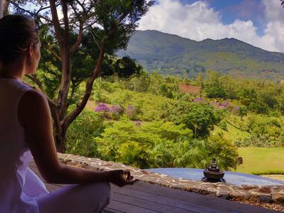 Žena medituje na terase s výhledem na zelenou krajinu a hory