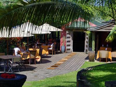 Außenbereich eines Restaurants mit Tischen, Stühlen, Sonnenschirmen und grüner Pflanzenumgebung.