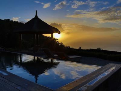 Ein Pavillon am Pool mit Sonnenuntergang und Himmel, der sich im Wasser spiegelt.