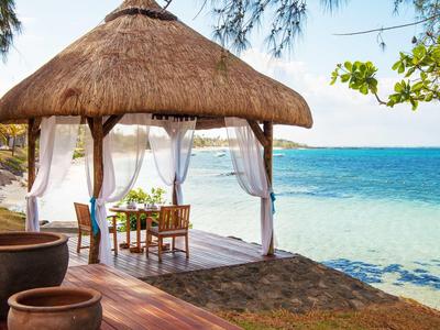 Offene Strandhütte mit Stühlen und Tisch, direkter Blick auf das blaue Meer.