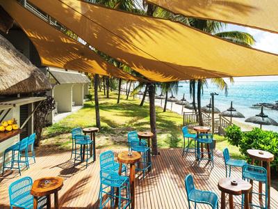 Terrasse eines Strandcafés mit blauen Stühlen und Tischen unter Sonnensegeln am Meer