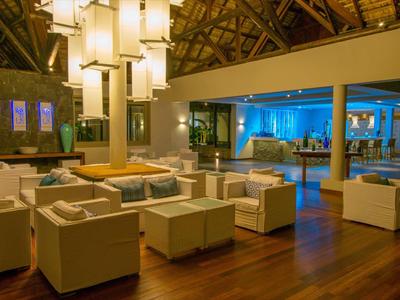 Modernes Hotel-Lounge mit weißen Sesseln, Holzboden und großen Lampen unter einer hohen Decke.