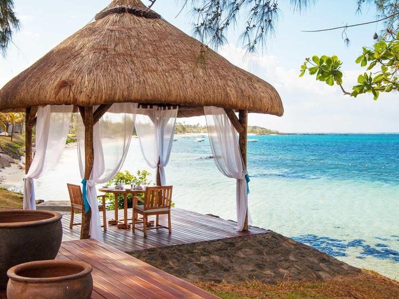 Otwarta plażowa chata ze strzechą i stolikiem z krzesłami nad morzem.