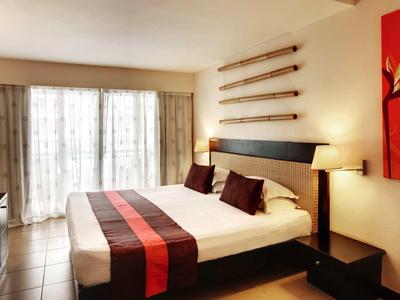 Camera moderna con grande letto, accenti rossi e grandi finestre con tende.