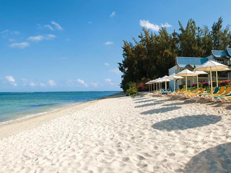 Spiaggia di sabbia bianca con ombrelloni e mare blu chiaro in una giornata di sole.