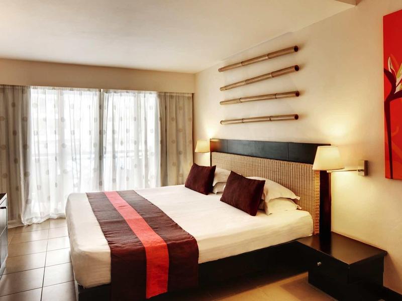 Camera moderna con grande letto, accenti rossi e grandi finestre con tende.