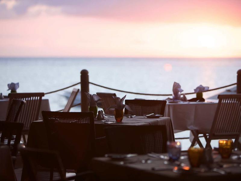 Tavoli e sedie vuoti su una terrazza con vista sul mare al tramonto.