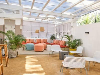 Helle Lounge mit bequemen Sitzsäcken, weißen Stühlen und Pflanzen unter Glasdach.