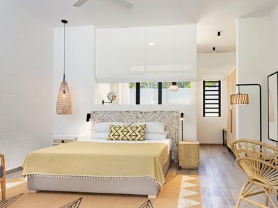 Helles Hotelzimmer mit Doppelbett, gelber Bettdecke, Rattanmöbeln und moderner Beleuchtung.