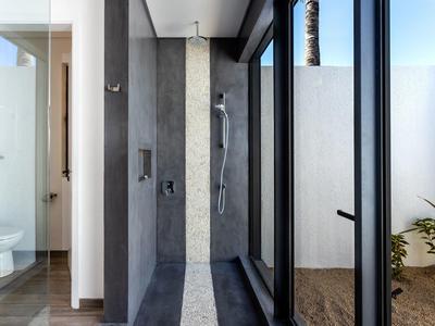 Moderner Außenbereich mit offener Dusche und großen Glasfenstern, Pflanzen deuten Garten an.