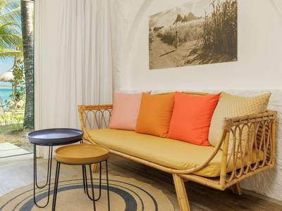 Przytulny kącik do siedzenia z plecioną drewnianą sofą i kolorowymi poduszkami obok okna z widokiem na morze.