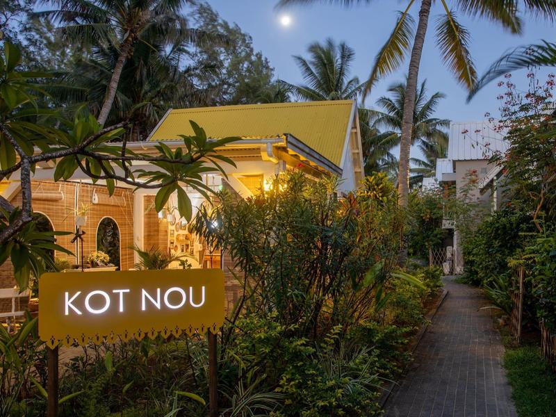 Tropikalna ścieżka hotelowa o zmierzchu z podświetlanym znakiem 'KOT NOU'.