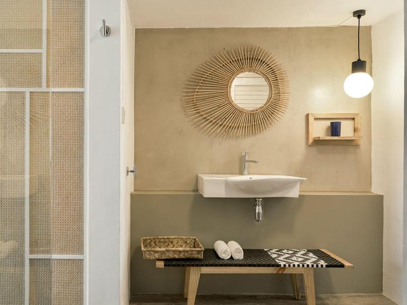 Nowoczesna łazienka z umywalką, okrągłym dekoracyjnym lustrem i drewnianą ławką z ręcznikami.