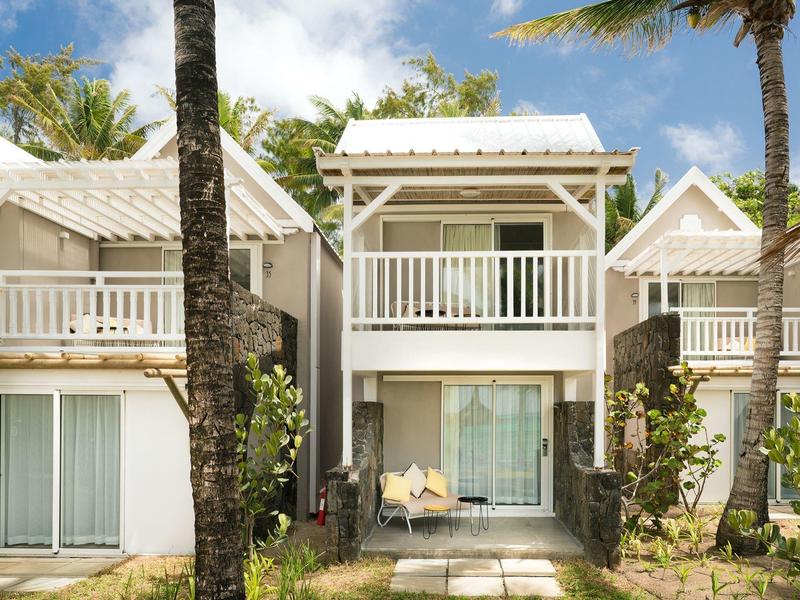 Dwupiętrowy budynek hotelowy z balkonami otoczony palmami i zielonym ogrodem