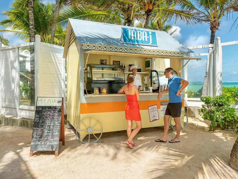 Mobilny bar z koktajlami na plaży z dwiema osobami w letnich ubraniach i palmami w tle.