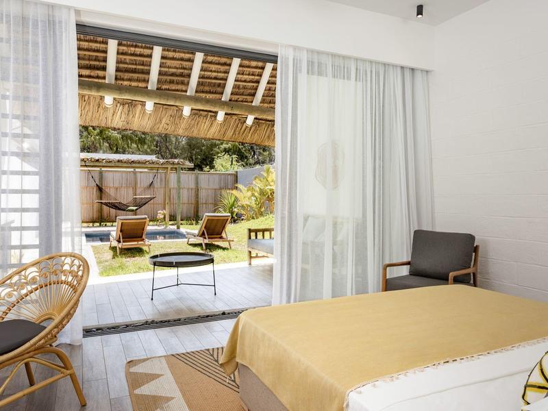 Jasny pokój hotelowy z podwójnym łóżkiem i przeszklonymi drzwiami przesuwanymi na zewnętrzny ogród z miejscem do siedzenia.