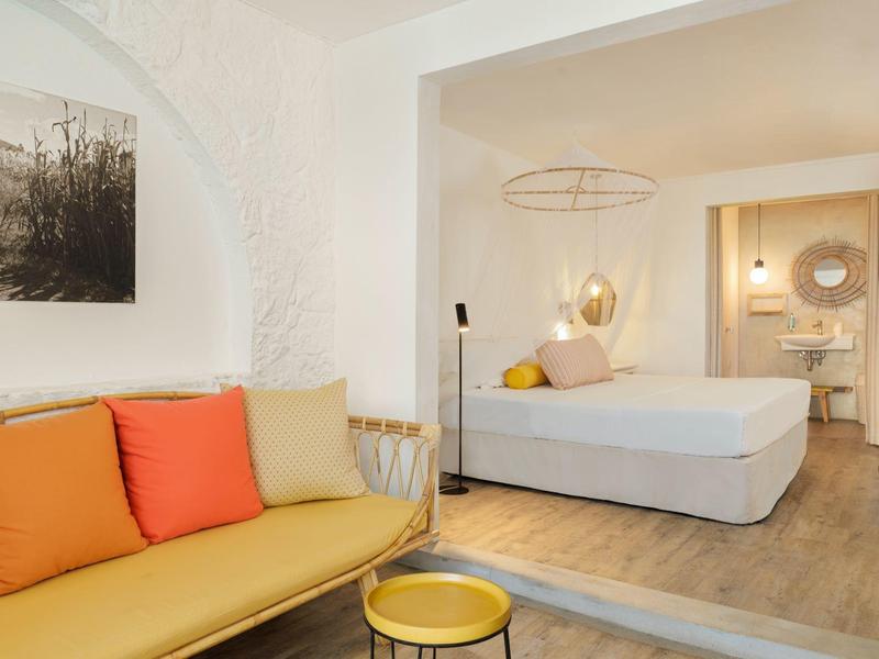 Nowoczesny pokój hotelowy z żółtą sofą, kolorowymi poduszkami i łóżkiem podwójnym.