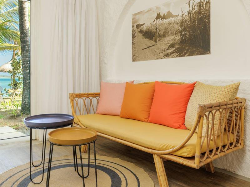 Przytulny kącik do siedzenia z plecioną drewnianą sofą i kolorowymi poduszkami obok okna z widokiem na morze.