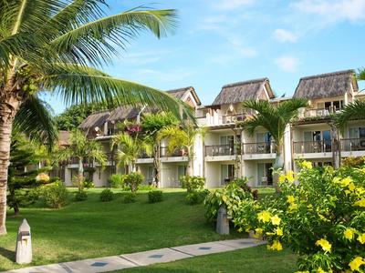 Hotel met tropische tuinen, palmbomen en heldere bloemen onder een blauwe lucht.