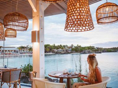 Frau sitzt auf einer Terrasse mit Körberlampen und Blick auf das Wasser.