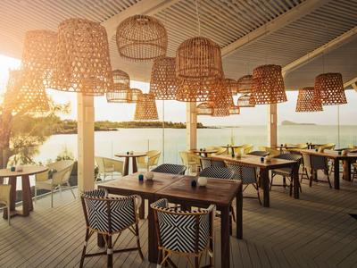 Open terras restaurant met tafels, stoelen en gevlochten lampen bij zonsondergang.