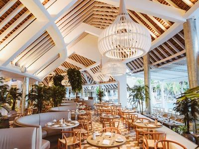 Elegant restaurant met houten meubels, witte plafondbalken en grote planten.