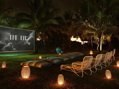 Gemütlicher Außenbereich mit Lounge-Stühlen und Laternen vor einer Leinwand in tropischer Nacht.