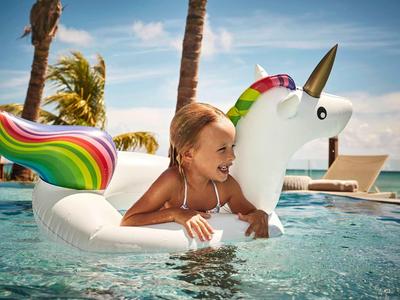 Kind ontspant op een eenhoorn opblaasbaar in het zwembad bij zonnig weer met palmbomen.
